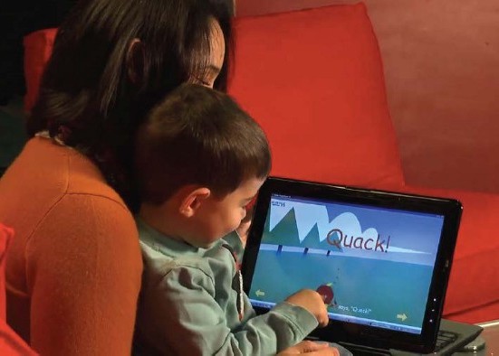 a mother sits with her son holding a tablet