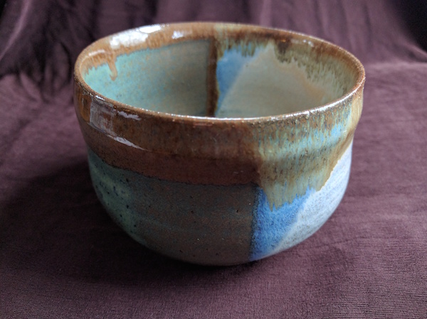 side view of a bowl with a rounded base and straight sides, glazed half sea green and half white, with brown along the rim