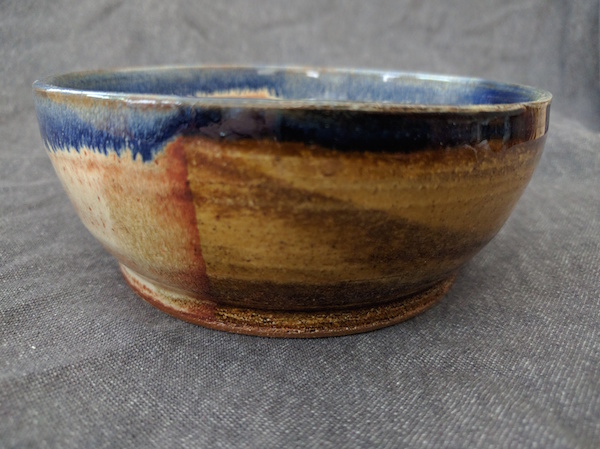 side view of a round marbled clay bowl, yellow-gold with a blue rim
