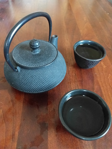 metal teapot on a table next to two matching round teacups