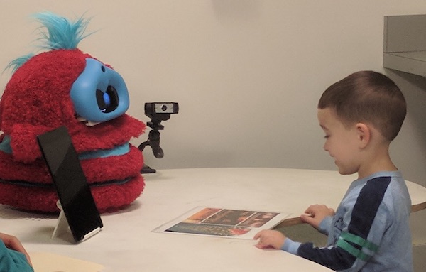 a boy sits across a table from a red and blue robot