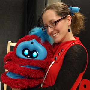 a woman in a red dress holding a red and blue striped robot and smiling