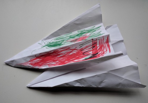 two paper airplanes, one has been colored on by a young child