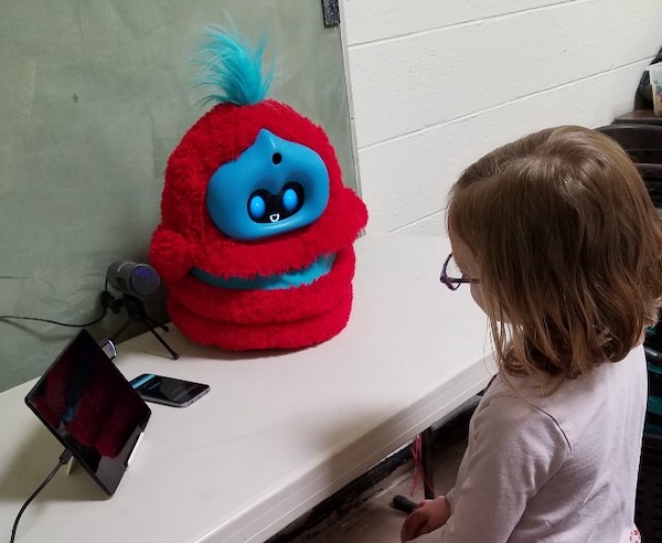 a child sits at a table that has a fluffy robot sitting on it