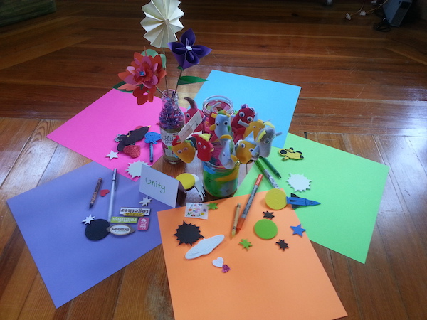 five colorful sheets of scrapbook paper arranged in a circle on the floor, with several jars in the middle containing a candle and paper flowers, with scrapbook materials scattered around