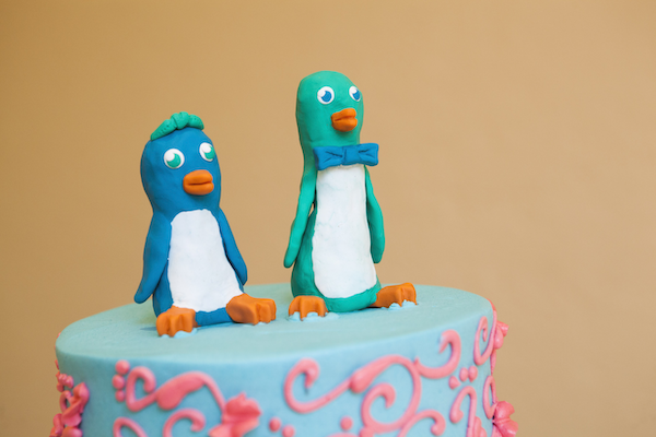 two colorful clay penguins sitting on top of a wedding cake