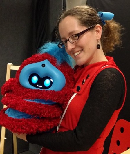 jacqueline holding the red and blue stripy fluffy tega robot, wearing a red dress