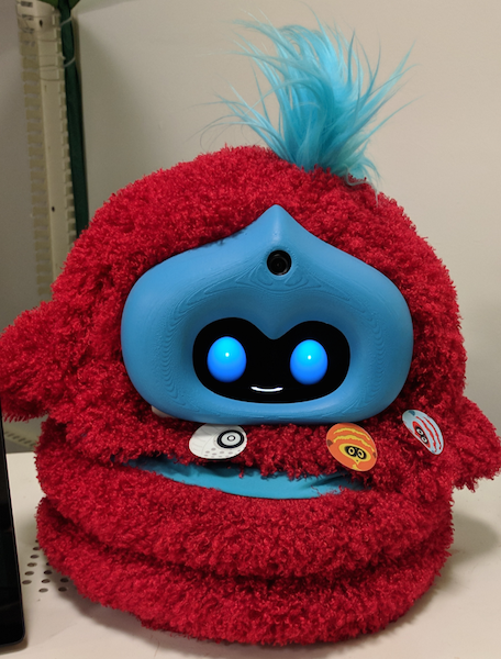 a fluffy red and blue tega robot with stickers stuck to its tummy