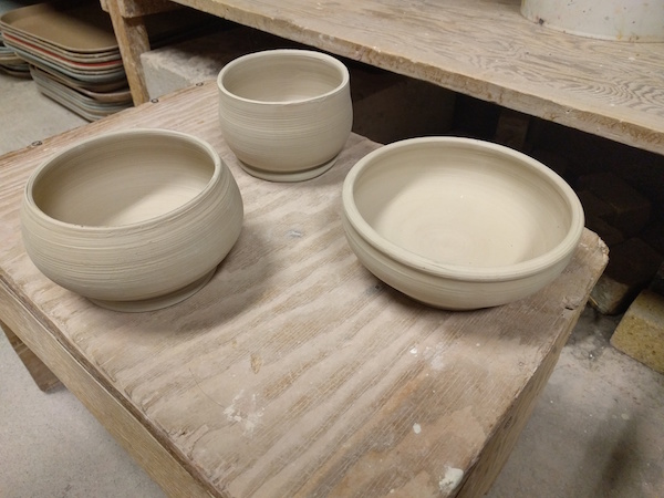 three white clay bowls sitting on a plank of wood