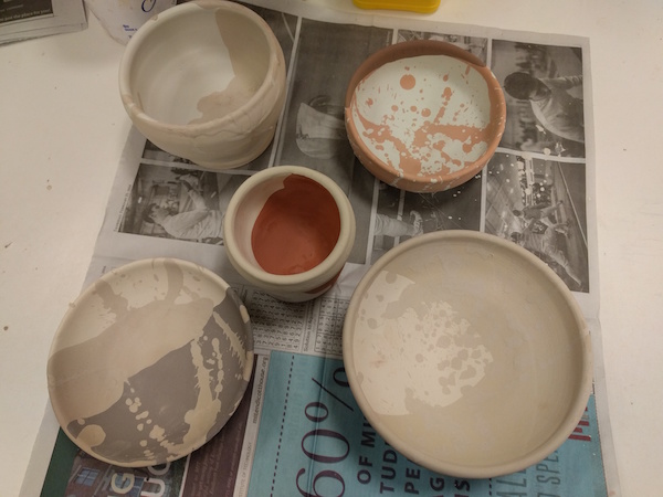 five glazed bowls before firing, in various dull shades of brown
