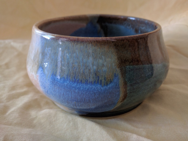 side view of a bowl with a round bulging base, fairly straight sides and a thin rim, glazed in browns and blues