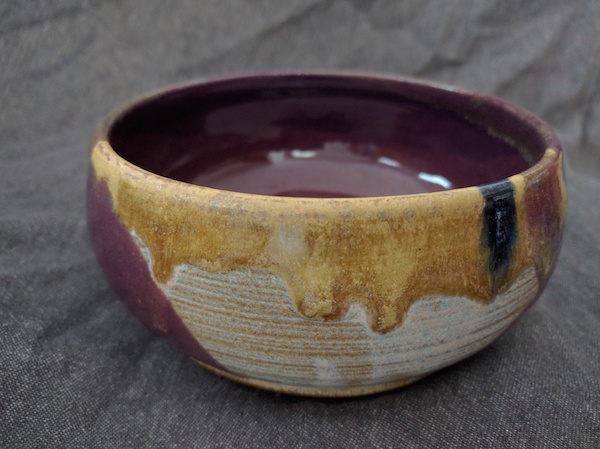 side view of a round, flat bowl, purple inside, white and yellow-gold matte outside