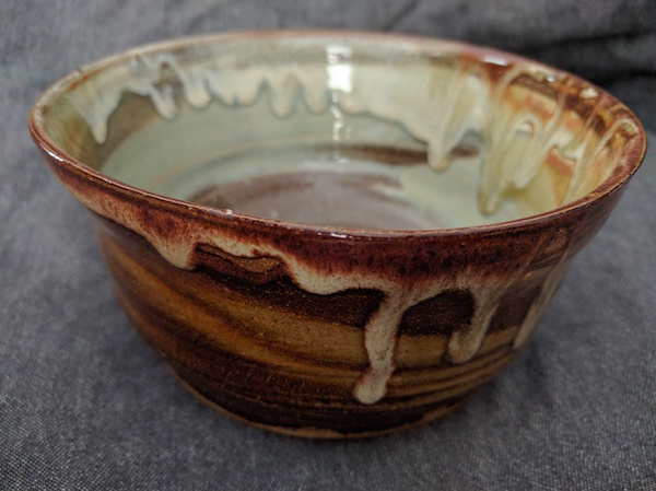 side view of a marbled clay bowl with gold and pale blue-green glazes, with a brown-white glaze dripping around the rim