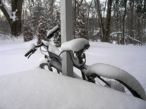 bicycle leaned against a porch, layers of snow on the handlebars, seat, and tires
