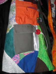 a zippered orange pocket above a flapped grey-green pocket on the side of the patchwork coat
