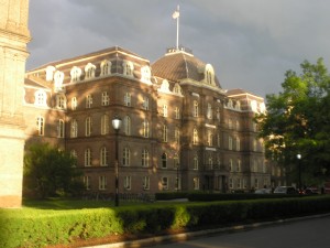 Main Building in June _big brick building in the sunlight, framed by dark thunderclouds and bright bits of green foliage_