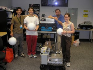 four people standing around a pair of boxy robots