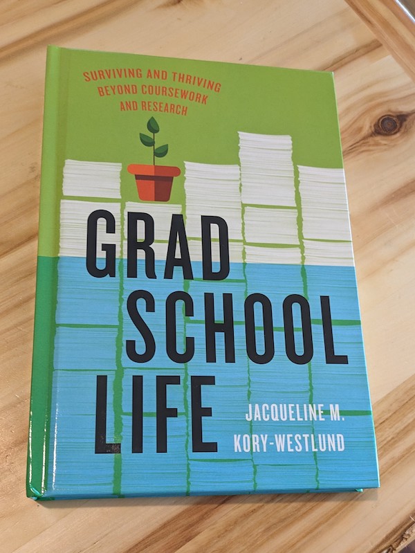 book Grad School Life: Surviving and Thriving Beyond Coursework and Research by Jacqueline M. Kory-Westlund. It shows a piles of papers behind the title, with a small potted plant on top of one stack, and the bottom half of the page covered in blue as if underwater