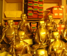 _several gold shiny buddha statues stacked in front of a set of box shelves_