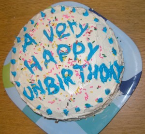 _white-frosted round cake with blue icing proclaiming "a very happy unbirthday!"_