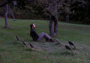 _man sitting on one of a series of folding chairs that are half-buried in the grass_