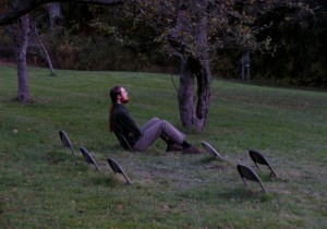 chair tops _man sitting on one of a series of folding chairs that are half-buried in the grass_
