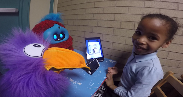 child smiling and looking up, beside fluffy robot and fluffy toucan puppet