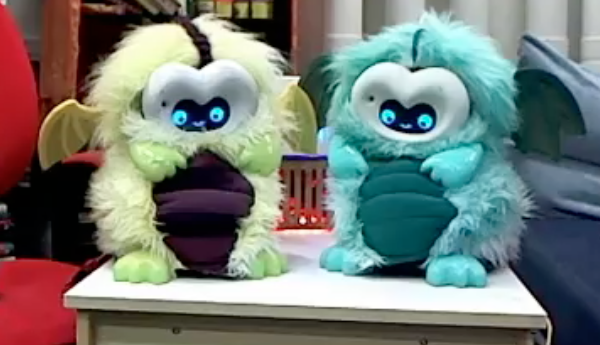 Two DragonBots a pair of bright, fluffy dragon robots sitting beside each other on a table
