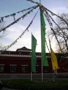 _Strings of prayer flags stretch out from the top of a pole in front of the temple with a sunset sky behind them_
