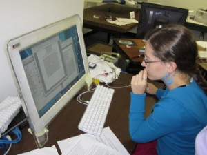 working on a paper girl in blue sweater sitting at a computer with documents open