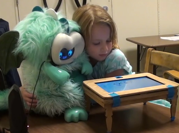 a young girl hugging a fluffy dragon robot behind a little play table