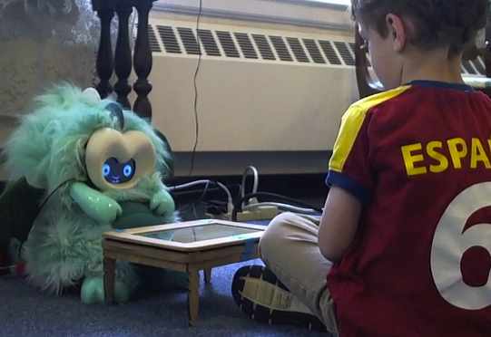 Child playing with storytelling robot Boy sitting on the floor across a mini table from a dragon robot, looking at the robot intently