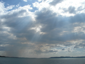 _sun beams through an array of puffy clouds over a grey-blue ocean_