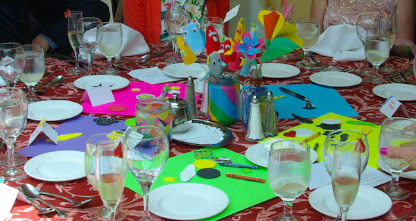 colorful sheets of scrapbook paper arranged in a circle on a table, with several jars in the middle containing a candle and paper flowers, with scrapbook materials scattered around