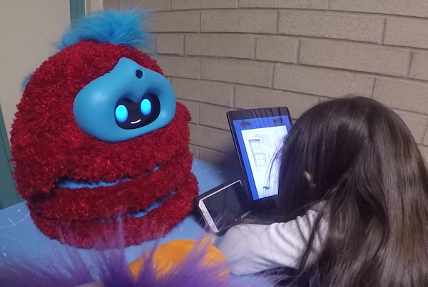 Tega tells a story fluffy robot tells a story to a child, who leans in over a tablet storybook listening
