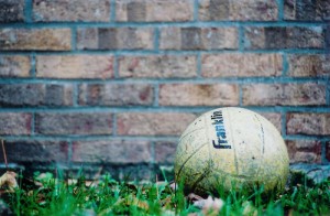 _volleyball sitting in grass beside a brick wall_